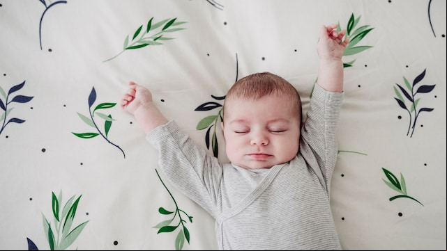 Bebé estirándose dormido en una cama con cara de felicidad