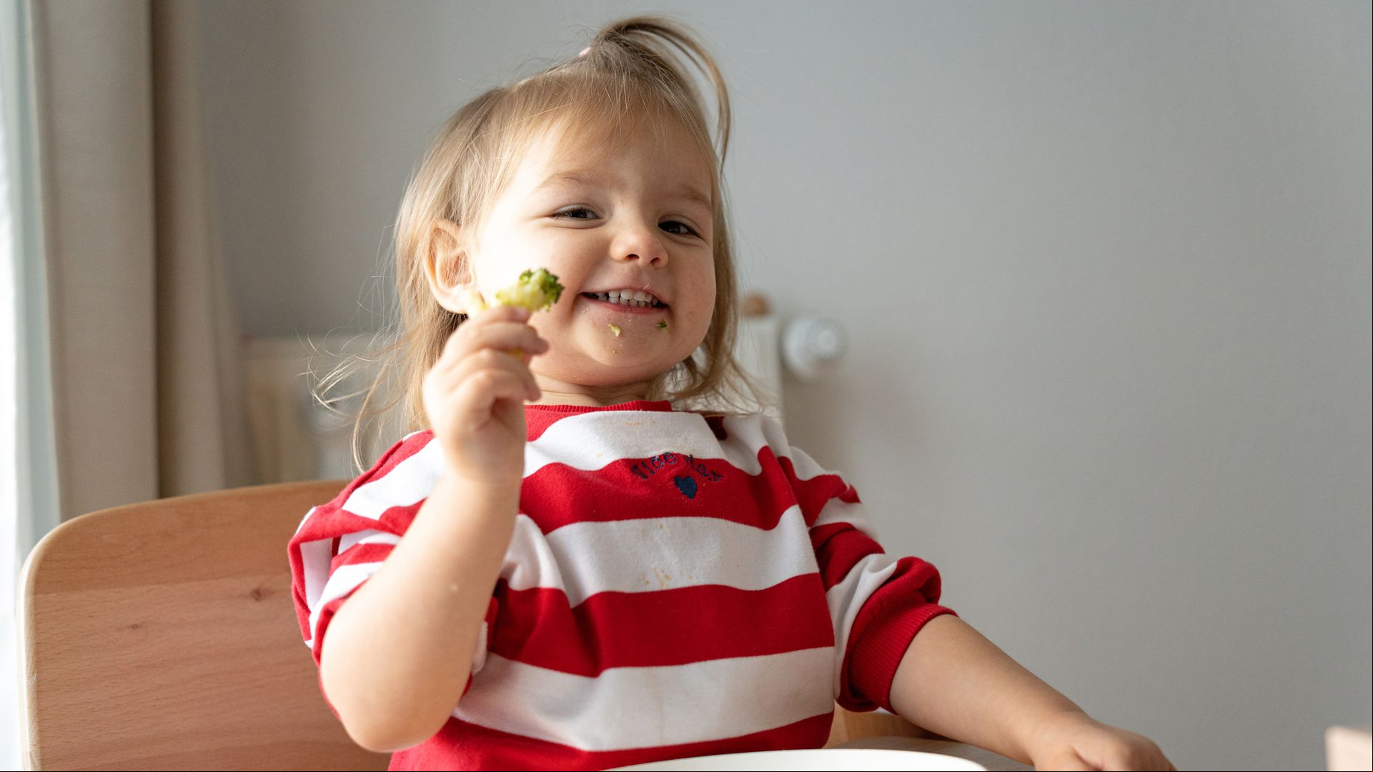 Niña come brócoli y sonríe