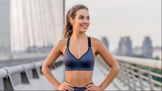 Chica después de correr en un puente sonriendo. Vientre plano y ropa deportiva.