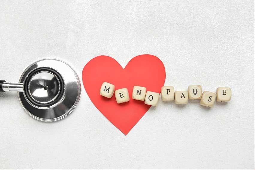 Palabra MENOPAUSIA con corazón de papel y estetoscopio sobre fondo blanco.