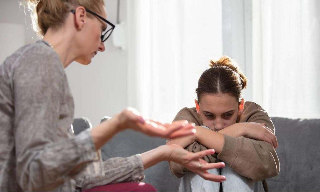 madre echando bronca a su hija adolescente sentada en el sof 
