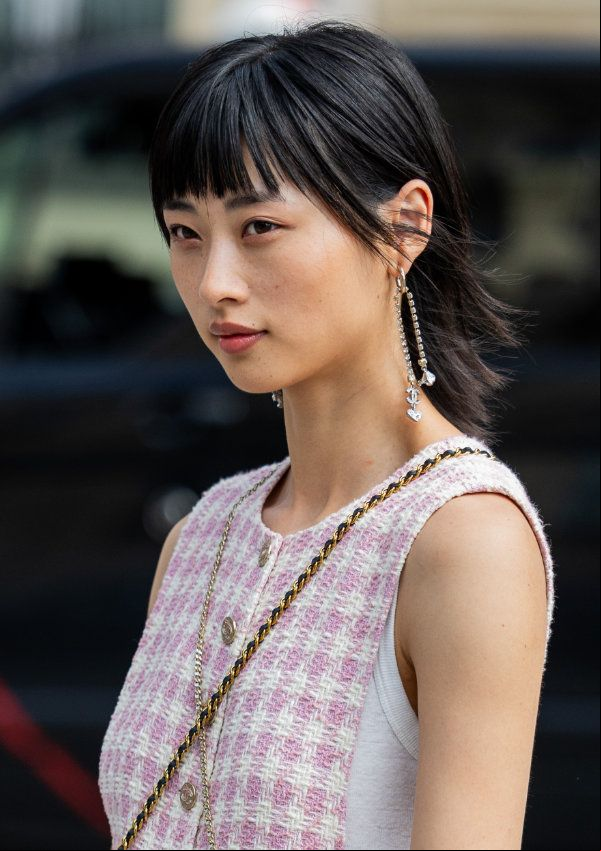 Mujer con corte de pelo mullet, pendientes colgantes y vestido rosa de tweed