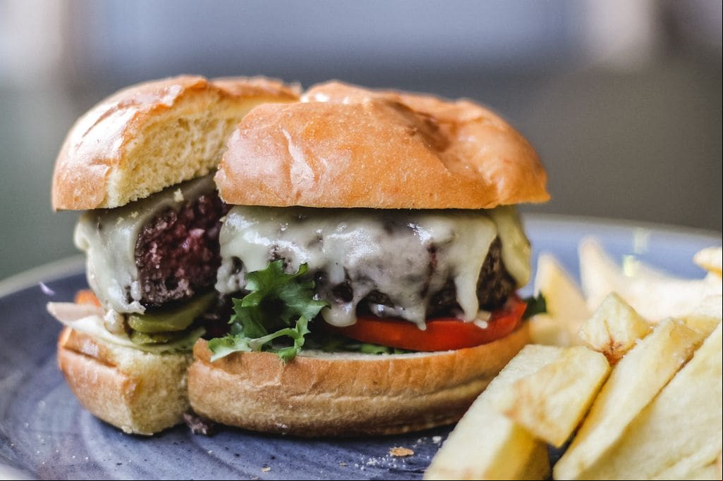 Hamburguesa de carne a la parrilla con queso, lechuga, pepinillo, rodajas de tomate y patatas fritas.
