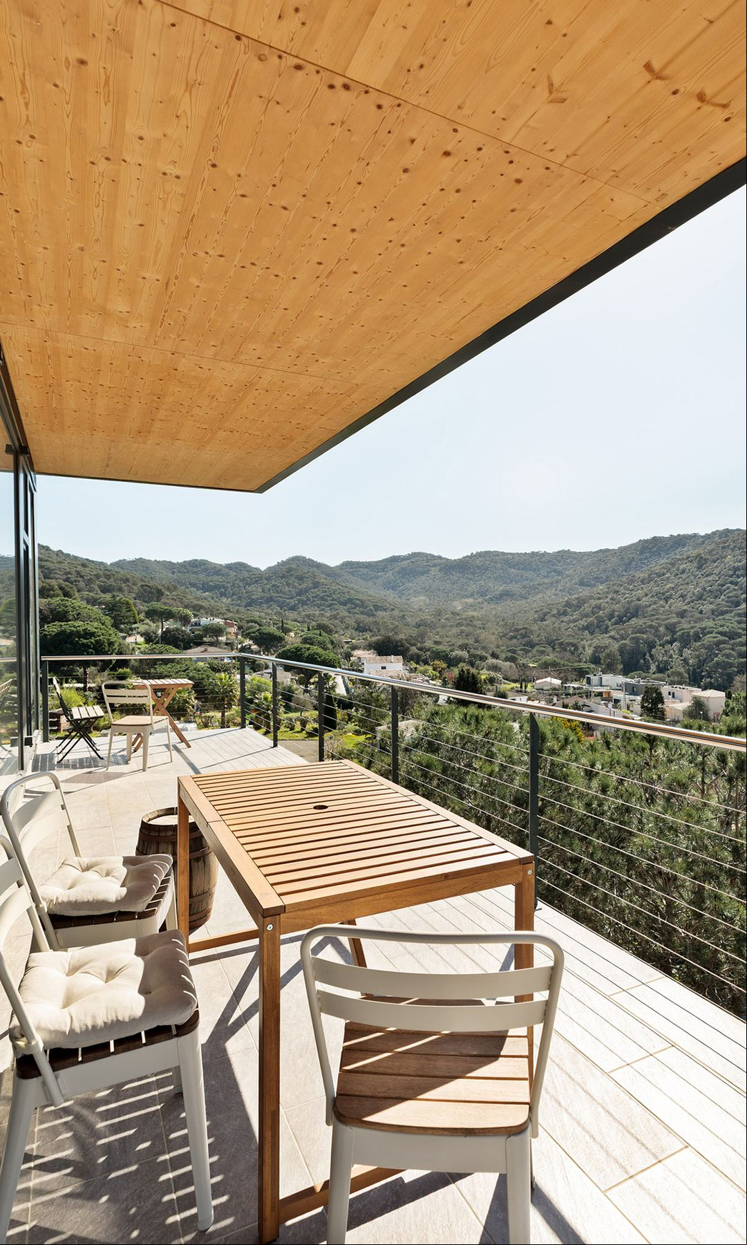 Terraza con vistas a un bosque con suelo y techo de madera, mesa de madera y sillas blancas