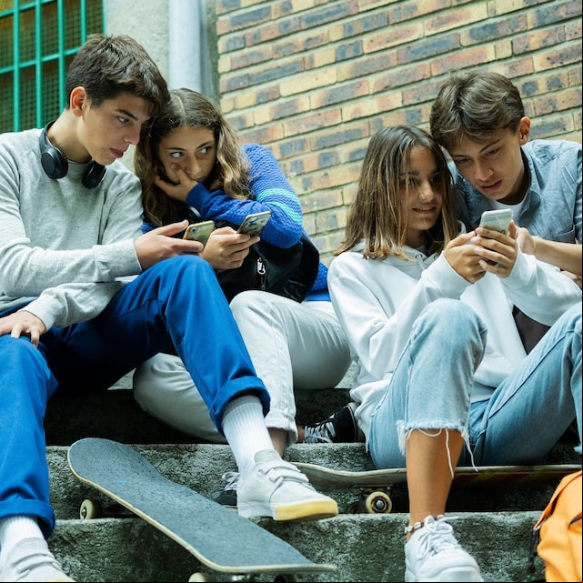 Adolescentes mirando sus móviles sentados sobre unos escalones a la entrada del instituto