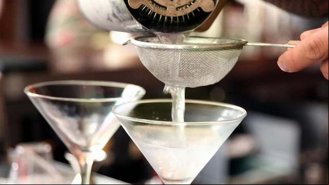 a bartender pouring martinis into chilled glasses through a small wire mesh strainer.