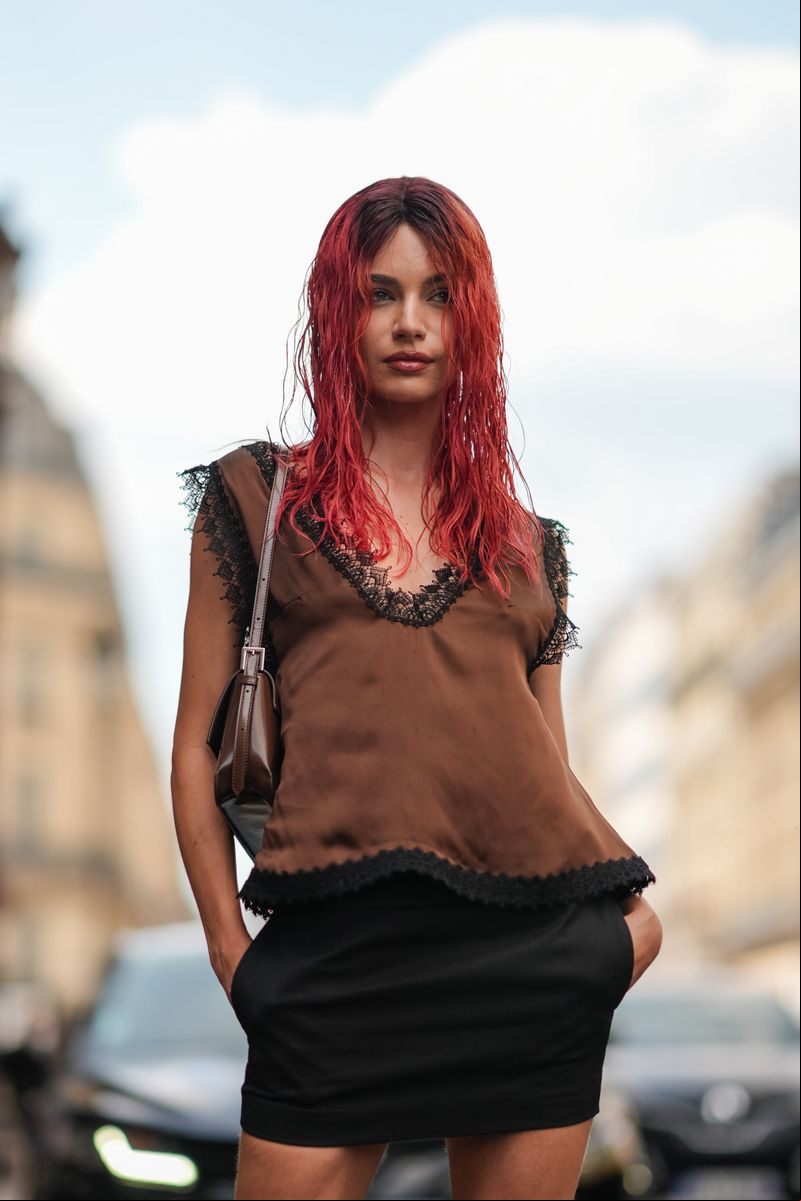 Mara Lafontan wears a dark brown satin black lace trimmed sleeveless shirt, dark brown leather bag, and black mini skirt outside Viktor & Rolf during the Paris Haute Couture Week Fall/Winter 2024-2025 on June 26, 2024, in Paris, . 
